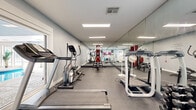 Located at 7627 E 37th St N in Wichita, Kansas, this well-appointed fitness center offers a comprehensive workout environment designed to support a wide range of exercise routines. The single-floor space is thoughtfully laid out, featuring durable rubber flooring throughout that provides both safety and comfort during exercise.

The room is equipped with an array of cardio machines, including treadmills and an elliptical trainer, as well as a multi-station cable machine and a rack of dumbbells in varying weights, making the space suitable for both cardiovascular and strength training workouts. Full-length mirrors line an entire wall, amplifying the sense of space and allowing users to monitor their form during exercise.

Overhead, recessed panel lighting provides bright, even illumination across the room. A motivational wall decal reading "If it doesn't challenge you, it won't change you" adds an energizing touch to the atmosphere. Yoga mats, resistance bands, and a stability ball round out the available accessories.

A standout feature of the fitness center is a large picture window that looks directly into an adjacent indoor pool area, complete with a vaulted ceiling and ample natural light — offering a visual connection to the broader recreational facilities. A door provides direct access to the pool area, creating a seamless transition between the two amenity spaces.