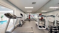 Located at 7627 E 37th St N in Wichita, Kansas, this well-appointed fitness center offers a comprehensive workout environment designed to support a wide range of exercise routines. The single-floor space is thoughtfully laid out, featuring durable rubber flooring throughout that provides both safety and comfort during exercise.

The room is equipped with an array of cardio machines, including treadmills and an elliptical trainer, as well as a multi-station cable machine and a rack of dumbbells in varying weights, making the space suitable for both cardiovascular and strength training workouts. Full-length mirrors line an entire wall, amplifying the sense of space and allowing users to monitor their form during exercise.

Overhead, recessed panel lighting provides bright, even illumination across the room. A motivational wall decal reading "If it doesn't challenge you, it won't change you" adds an energizing touch to the atmosphere. Yoga mats, resistance bands, and a stability ball round out the available accessories.

A standout feature of the fitness center is a large picture window that looks directly into an adjacent indoor pool area, complete with a vaulted ceiling and ample natural light — offering a visual connection to the broader recreational facilities. A door provides direct access to the pool area, creating a seamless transition between the two amenity spaces.