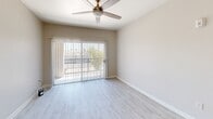 Located in Phoenix, AZ, this single-floor, one-bedroom, one-bathroom residence offers a thoughtfully organized layout across five distinct spaces: a living room, bedroom, kitchen, bathroom, and hallway. The living room is bright and open, featuring light wood-style flooring, a ceiling fan, and a sliding glass door with vertical blinds that leads to an outdoor area and fills the room with natural light. The kitchen is efficiently designed in a U-shaped configuration, outfitted with white cabinetry, light countertops, and a suite of appliances including a black electric range, stainless steel microwave, black refrigerator, and dishwasher, all set on matching light wood-style flooring. The spacious bedroom is carpeted for comfort and includes a ceiling fan, a window with natural light, and a walk-in closet complete with built-in shelving and a hanging rod, offering generous storage. The bathroom features wood-style tile flooring, a single-sink vanity with white cabinetry, a large mirror, and a tub-shower combination. Neutral warm-beige walls are carried consistently throughout the space, creating a cohesive and clean aesthetic well-suited to the Phoenix climate.