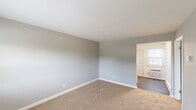 Located at 4128 Firwood Ln in Charlotte, NC, this two-bedroom, one-bathroom unit offers a practical and efficient single-floor layout. The kitchen is outfitted with white shaker-style cabinetry, light countertops, a coil-top electric range, a full-size refrigerator, and a stainless steel sink. Wood-look flooring runs throughout the kitchen and entry areas, while natural light enters through a window fitted with blinds. A wall-mounted HVAC unit provides climate control in the kitchen area. Both bedrooms feature neutral gray walls, wall-to-wall carpet, and flush-mount ceiling light fixtures. The spacious primary bedroom includes a double-door closet and direct sightlines to the kitchen, while the secondary bedroom benefits from a window with a window-unit air conditioner and a baseboard heater. The full bathroom is cleanly finished with white subway tile surrounding the tub-shower combination, a rain-style showerhead with chrome fixtures, and a privacy window. The overall aesthetic is clean and understated, with a consistent neutral palette of whites and grays carried throughout the home. A dedicated closet provides additional storage, completing the functional layout of this Charlotte residence.
