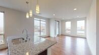This well-appointed upper-floor unit offers a thoughtfully designed open-concept layout that seamlessly connects the kitchen, dining, and living areas. Warm hardwood flooring flows throughout the main living spaces, while large windows on multiple walls flood the interior with natural light and frame sweeping city views.

The kitchen is a standout feature, equipped with sleek dark cabinetry, granite countertops, a central island with an undermount sink, and a full suite of stainless steel appliances including a refrigerator, electric range, built-in microwave, and dishwasher. Stylish pendant lighting illuminates the island, adding a contemporary touch. A stacked in-unit washer and dryer is conveniently located nearby.

The spacious living area benefits from recessed lighting and generous window exposure, creating a bright and airy atmosphere with urban views. The bedroom is finished with plush carpeting, a ceiling fan, and a large picture window that continues the city backdrop. The bathroom is clean and functional, featuring a soaking tub with shower combination, dark vanity cabinetry, and neutral tile flooring. Overall, the space presents a modern, urban aesthetic with quality finishes throughout.