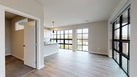 Located at 114 E Main St in Waunakee, WI, this contemporary single-floor residence offers a thoughtfully designed open-concept layout bathed in natural light. The living and dining area is anchored by striking floor-to-ceiling black-framed windows that frame views of the surrounding downtown streetscape, creating a bright and airy atmosphere throughout. Light-toned luxury vinyl plank flooring flows seamlessly across the main living spaces, complementing the neutral color palette.

The kitchen is a standout feature, boasting white shaker-style cabinetry, a white subway tile backsplash, dark countertops, and a generous island with pendant lighting overhead. Stainless steel appliances, including a refrigerator, range, microwave, and dishwasher, complete the functional and stylish cooking space. A pass-through window connects the kitchen to an adjacent space, enhancing the open feel.

The primary bathroom features a dual-sink vanity with white cabinetry, dark countertops, and a large mirror with vanity lighting, paired with light tile flooring. A second bathroom offers a single-sink vanity with ample storage and wood-look flooring. A spacious walk-in closet with wire shelving and carpeted flooring provides generous storage. A sliding barn door and access to a private outdoor deck round out this well-appointed residence.