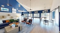 Located at 100 Reflections Circle in Casselberry, Florida, this single-floor community clubhouse offers a generously sized, thoughtfully designed gathering space defined by bold cobalt blue accent walls, crisp white shiplap paneling, and warm wood-look flooring throughout. Soaring vaulted ceilings fitted with multiple ceiling fans lend an airy, open feel to the expansive main living area, which serves as the centerpiece of the space.

The main hall is anchored by a full-size pool table and complemented by eclectic, modern furnishings including leather lounge chairs, area rugs, and stylish side tables — creating an inviting atmosphere for socializing and recreation. A foosball table and bar-height seating area with a kitchenette further enhance the entertainment offerings. Elevated by a short staircase, this secondary lounge zone features a patterned accent wall and pendant lighting, adding architectural interest.

A quieter lounge nook, partitioned by a sliding barn-style door, offers a more intimate workspace setting with a built-in desk, arched window, and pool views. The entrance and hallway areas are bright and welcoming, with shiplap walls, large-format artwork, and curated décor setting the tone upon arrival. Large windows along the rear of the space frame outdoor views and flood the interior with natural light.