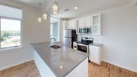 This single-floor residence offers a thoughtfully designed open-concept layout with clean, modern finishes throughout. The entryway welcomes you with warm hardwood flooring that extends through the main living areas, leading into a spacious living room bathed in natural light from multiple large windows framing elevated city views. Ceiling fans are present throughout, adding both function and a subtle design element.

The kitchen is a standout feature, showcasing a large central island with a polished granite countertop and an undermount sink, complemented by decorative pendant lighting overhead. White shaker-style cabinetry, including glass-front upper cabinets, pairs with a classic subway tile backsplash and stainless steel appliances, including a refrigerator, electric range, and built-in microwave.

The bedrooms are carpeted for comfort, each equipped with a ceiling fan and windows offering city views. One bedroom features mirrored sliding closet doors, while another benefits from a large corner window.

Two bathrooms serve the unit. The primary bathroom includes a frameless glass walk-in shower, white cabinetry, and a dark granite vanity countertop with pendant lighting. The secondary bathroom features a tub-shower combination and a matching granite countertop vanity, maintaining a consistent modern aesthetic throughout.