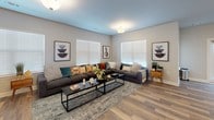 Located in Lebanon, Tennessee, this single-floor community space is thoughtfully designed for both relaxation and social gatherings. The layout flows seamlessly across several distinct functional areas, all unified by warm hardwood-style flooring and a neutral color palette.

The expansive lounge area is anchored by a generous sectional sofa adorned with colorful accent pillows, centered around a sleek black coffee table atop a textured area rug. Multiple large windows fitted with white blinds allow abundant natural light to fill the room, creating a bright and welcoming atmosphere. Framed artwork decorates the walls, adding character to the space.

The kitchen is a standout feature, showcasing dark espresso cabinetry, stainless steel appliances including a French door refrigerator and range, and a large granite-topped island with seating for several. Pendant lighting hangs above the island, while a dining table nearby offers additional seating for casual meals.

The recreation and dining area is defined by striking whitewashed brick accent walls that lend a rustic, industrial character to the space. Multiple dark dining tables with black spindle chairs provide ample group seating, while a full pool table with a mounted cue rack serves as a central entertainment feature. French doors offer access to the exterior, further enhancing the open, connected feel of this versatile community hub.