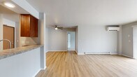Located at 1630 Fordem Ave in Madison, Wisconsin, this single-floor residence offers a well-designed layout with a clean, neutral aesthetic throughout. The open living area is finished with light wood-tone laminate flooring and features large sliding glass doors with vertical blinds that allow generous natural light and outdoor views. A wall-mounted air conditioning unit and baseboard heating provide year-round climate control. The kitchen is positioned adjacent to the living space in a semi-open layout, featuring rich dark wood cabinetry, granite-style countertops, a stainless steel sink, and a dishwasher. A dedicated utility area off the kitchen houses a stacked washer unit and refrigerator, adding practical convenience. The bedrooms are carpeted for comfort and include windows with blinds that bring in natural light, along with baseboard heating. The unit includes two bathrooms, each featuring warm wood vanities, white countertops, tiled shower-tub combinations, and brushed nickel fixtures and grab bars. A ceiling fan is installed in the main living or dining area, enhancing airflow. The overall interior is finished in soft gray tones with clean white trim, creating a bright, cohesive, and move-in-ready living environment.