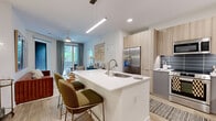 Located at 622 Merritt Ave in Nashville, TN, this contemporary two-bedroom, two-bathroom residence offers a well-designed single-level floor plan with modern finishes throughout. The open-concept kitchen anchors the living space and is outfitted with stainless steel appliances, including a refrigerator, range, and microwave. Light wood cabinetry pairs with gray lower cabinets, complemented by a slate-toned tile backsplash and crisp white quartz countertops. A kitchen island with an integrated sink and seating provides a functional and social focal point, while light wood-style flooring flows seamlessly into the living area. Natural light filters through large windows dressed with sheer curtains, lending an airy ambiance to both bedrooms. The primary bedroom features a window-lined wall and connects to a full en-suite bathroom with a dual-sink vanity, wood-toned cabinetry, white quartz counters, large-format tile flooring, and a glass-enclosed shower. A second full bathroom offers a tiled tub-shower combination and matching vanity. Both bedrooms are served by generously sized walk-in closets with wire shelving systems that maximize storage. The overall design reflects a clean, contemporary aesthetic well-suited to modern urban living in Nashville.