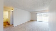 This single-floor unit is designed with a straightforward, functional layout that makes efficient use of its available space. The entryway greets residents with warm wood-look flooring that extends through the hallway and into the kitchen, providing a practical and easy-to-maintain surface in high-traffic areas.

The living area is a generously sized, open room finished with neutral wall-to-wall carpeting that adds comfort underfoot. A textured ceiling runs overhead, and a large sliding glass door fitted with vertical blinds allows natural light to fill the space while providing direct outdoor access and views of the surrounding greenery.

The kitchen is positioned adjacent to the living space and features white cabinetry, a built-in range, sink, and dishwasher. Wood-look flooring continues throughout this area, and a pendant light fixture provides overhead illumination.

The bedroom is a well-proportioned room with carpeted flooring, a window with vertical blinds admitting natural light, and a built-in closet with bifold doors offering practical storage. The bathroom includes a full tub and shower combination with clean white tile surround and chrome fixtures, maintaining the unit's consistent neutral aesthetic throughout.