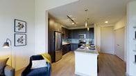 This 1-bedroom, 1-bathroom residence offers a thoughtfully designed single-floor layout that maximizes both function and style. The open-concept living and kitchen area creates a seamless flow, anchored by a striking kitchen outfitted with dark espresso cabinetry that extends to the ceiling, a light-toned quartz countertop island with pendant lighting overhead, and a full suite of stainless steel appliances including a refrigerator, microwave, and range. A subway tile backsplash in a soft blue-grey hue adds a contemporary touch to the kitchen's refined aesthetic. Track lighting illuminates the space efficiently, complementing the warm wood-look flooring that runs throughout the main living areas. The kitchen island doubles as a dining space, providing a casual yet elegant setting. The living area flows naturally from the kitchen, offering room for comfortable seating and everyday relaxation. Clean white walls and neutral tones create a bright, airy ambiance, while the overall layout ensures efficient use of every square foot. The unit's modern finishes and cohesive design make it a polished and practical living space.