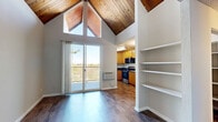 Located at 1160 Lincoln Ave in Walnut Creek, CA, this efficiently designed single-floor unit makes a striking first impression with its soaring vaulted ceiling clad in warm natural wood planks — a standout architectural feature that adds volume and character well beyond the unit's compact footprint. Large triangular clerestory windows at the peak of the vault flood the living area with abundant natural light, enhancing the open, airy atmosphere.

The living area is anchored by rich hardwood-style flooring that runs throughout and opens directly to a private balcony through a full-height sliding glass door, offering pleasant outdoor views of the surrounding greenery. A built-in white shelving unit provides practical display and storage space along one wall, while a wall-mounted heater/AC unit ensures year-round comfort.

The kitchen is well-appointed with warm honey-toned cabinetry, dark granite countertops, stainless steel appliances including a refrigerator, electric range, and over-the-range microwave, and a stainless steel sink. A small chandelier adds a decorative touch to the adjacent dining nook area.

The closet provides dedicated storage space, and a six-panel entry door with textured wall finishes completes the unit. Clean neutral tones throughout create a cohesive, move-in-ready environment.