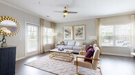 This thoughtfully designed single-floor unit in Columbia, SC presents an open-concept layout that maximizes its well-utilized footprint. The living room is bright and welcoming, featuring hardwood-style flooring, crown molding, a ceiling fan, and multiple windows fitted with plantation shutters and sheer draping that invite generous natural light. A sliding glass door provides access to an outdoor balcony, further enhancing the airy atmosphere.

The kitchen is equipped with rich dark wood cabinetry, granite countertops, black appliances, and a peninsula with bar seating illuminated by pendant lighting—seamlessly connecting to the dining area. The dining space features warm-toned walls and stylish gold metallic wall art, creating a distinct and sophisticated ambiance.

The bathroom includes tile flooring, dark wood vanity cabinetry with stone countertops, and a full mirror. A dedicated laundry area houses a full-size washer and dryer. Throughout the unit, hardwood-style flooring, neutral gray walls, crown molding, and gold accent details contribute to a cohesive, contemporary aesthetic.