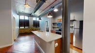Located at 900 Goss Ave in Louisville, Kentucky, this 2-bedroom, 2-bathroom loft blends historic industrial character with modern updates. The open-concept living and kitchen area immediately impresses with soaring ceilings, exposed ductwork, and original wide-plank hardwood floors that speak to the building's rich heritage. Exposed brick and stone walls add texture and warmth throughout, while tall arched windows flood the space with natural light and lend an architectural elegance typical of adaptive reuse buildings.

The kitchen is a standout feature, anchored by a granite-topped island with a built-in sink and pendant lighting overhead. Warm wood cabinetry, stainless steel appliances — including a range, microwave, and refrigerator — and open shelving complete the functional yet stylish kitchen layout.

Both bedrooms carry the same character-rich aesthetic, with hardwood floors and large windows framed by exposed brick. The two bathrooms are clean and functional, each featuring wood-toned vanities and shower facilities. A dedicated laundry area houses a stacked washer and dryer unit alongside a water heater for added convenience. A hallway and closet round out the layout, making this a well-organized, character-filled urban residence.