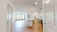 Located at 5750 Airport Rd in Santa Fe, NM, this thoughtfully designed one-bedroom, two-bathroom residence offers a clean, modern aesthetic with high-quality finishes throughout. The open-concept kitchen and living area serves as the heart of the home, anchored by a large center island with a white quartz countertop, pendant lighting with gold accents, and a suite of stainless steel appliances. The kitchen features a two-tone cabinet design — crisp white upper cabinets paired with gray lower cabinets — complemented by a marble-style tile backsplash. Light hardwood flooring flows seamlessly through the main living areas, enhancing the bright, airy ambiance. The living room opens to a private balcony through a glass door, allowing natural light to pour in alongside views of the surrounding area, with a ceiling fan adding comfort overhead. The bedroom is carpeted for warmth and comfort, offering a quiet retreat. Both bathrooms are well-appointed with gray vanity cabinetry, white quartz countertops, and modern fixtures; the primary bath includes a glass-enclosed shower and direct access to a walk-in closet. The overall design is contemporary and cohesive, making efficient use of the available space.