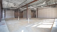 Located at 215 Monticello Ave in Williamsburg, Virginia, this single-story commercial shell space presents a blank canvas for a prospective tenant or developer. The space is currently in its pre-construction state, with exposed earth floors, structural steel columns, and visible overhead infrastructure including conduit runs, ductwork, and plumbing rough-ins already in place — providing a strong foundation for future buildout.

The front of the space features expansive floor-to-ceiling storefront glazing with multiple large window bays and glass entry doors, flooding the interior with abundant natural light and offering clear sightlines to the surrounding streetscape. Corner glazing further enhances the sense of openness and visibility from Monticello Ave.

The interior is subdivided into a large open main area supported by structural steel columns, with partially framed secondary spaces toward the rear, delineated by concrete masonry unit walls and drywall partitions. Reflective foil insulation lines portions of the perimeter walls, and plumbing stubs are visible in the back sections, suggesting areas designated for restroom or utility use.

The exposed ceiling deck reveals a metal pan system supported by steel framing, lending the space an industrial character. Its location within an active mixed-use development positions it well for retail, restaurant, or service-oriented use.