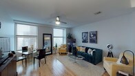 The Marlon Brando is a thoughtfully designed 2-bedroom, 2-bathroom residence that offers a comfortable and stylish single-floor layout. Warm hardwood flooring flows throughout the open living areas, anchoring a spacious living room filled with natural light from large windows that frame city views. A ceiling fan adds a functional accent overhead, while the open sightlines connect the living space to the dining area seamlessly.

The kitchen features dark wood cabinetry, white quartz countertops, a double stainless steel sink, and a striking metallic tile backsplash. Stainless steel appliances, including a built-in microwave and gas range, complete this well-equipped culinary space.

Both bedrooms are generously proportioned with hardwood floors and ceiling fans. The primary bedroom includes a private en-suite bathroom featuring a walk-in glass-enclosed shower with large-format tile. The second bathroom offers a tub-shower combination with tile surround and a vanity topped with granite countertops.

Throughout the residence, neutral gray walls provide a clean, contemporary backdrop. The layout, as seen in the dollhouse view, is efficiently organized with in-unit laundry and well-defined living zones, making this a highly functional and stylish urban residence.