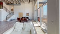 Penthouse 31 at 550 Seagaze in Oceanside is a two-story residence defined by dramatic architectural details and an abundance of natural light. The main living level showcases soaring double-height ceilings with exposed industrial ductwork, creating a loft-like ambiance that feels both spacious and distinctive. Floor-to-ceiling glass walls and oversized sliding doors flood the open-plan living and dining area with sunlight and frame sweeping elevated views of the surrounding cityscape and beyond. The living space connects seamlessly to an outdoor area, enhancing the indoor-outdoor flow.

Two well-appointed kitchens are present across the unit — one featuring light grey cabinetry, stone countertops, stainless steel appliances including a built-in oven, cooktop, and microwave, complemented by light hardwood flooring. A second kitchen offers a similarly clean, contemporary design with matching cabinetry and integrated dishwasher. The bathrooms are finished with large-format white tile, combination tub-shower fixtures, and clean modern vanities.

A private office or flex space features elegant wood-framed shoji-style sliding panels, offering a refined, tranquil setting. A staircase connects both levels, and wood-look flooring runs throughout, tying the home's modern, airy aesthetic together cohesively.