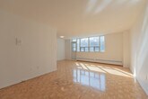 Located at 30 Carabob Ct in Toronto's Scarborough district, this single-floor, one-bedroom, one-bathroom unit offers a thoughtfully organized layout across a comfortable footprint. The space is unified by warm parquet wood flooring throughout the living areas and bedroom, a classic detail that adds texture and character to each room.

The living room is a standout feature, benefiting from a large multi-pane window wall that frames outdoor greenery and fills the room with abundant natural light. Baseboard heating runs beneath the windows, and the clean white walls create a bright, open ambiance. The sunlight casts dynamic patterns across the parquet floor, enhancing the room's welcoming atmosphere.

The galley-style kitchen is efficiently designed with white cabinetry, subway tile backsplash, and white tile flooring. It is equipped with stainless steel appliances including a refrigerator, electric stove, microwave, and dishwasher, along with ample counter and storage space along both sides.

The bedroom is a well-proportioned private retreat featuring parquet flooring, a sliding mirrored closet, and clean white walls. The bathroom is finished with white subway-style wall tiles and includes a full soaking tub with an overhead shower, conveying a crisp, clean aesthetic throughout.