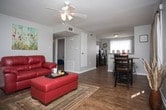 This single-story residence in Harvey, Louisiana, offers a well-organized layout across several distinct living spaces. The living room serves as a central gathering area, featuring rich hardwood-style flooring, a textured ceiling with a ceiling fan, and ample natural light from a window. A bold red leather sofa and ottoman anchor the room, complemented by a decorative console table along the wall.

Adjacent to the living room, the dining area accommodates a round dining table with chairs and bench seating, positioned near a window with linen drapes that allow natural light to filter in. The kitchen is equipped with black appliances, including a range and dishwasher, set against light-toned cabinetry and granite-look countertops. A metallic tile backsplash adds a distinctive visual element, and a window above the sink provides additional light.

The primary bedroom is generously proportioned, featuring plush carpeting, a textured ceiling, and patterned window treatments. A second bedroom comfortably fits two twin beds with carpeted flooring and blue curtains, while a third bedroom offers carpeted floors and natural light. The bathroom includes a tub-shower combination with tile surround and hardwood-style flooring.