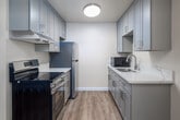 Located in Poway, CA, this well-designed single-story, one-bedroom, one-bathroom residence makes smart use of its compact footprint. The open kitchen is a standout feature, showcasing a galley-style layout with grey shaker cabinetry, white quartz countertops, stainless steel appliances including an electric range and refrigerator, and light wood-style vinyl flooring that extends into the adjoining dining and living area. A modern ring-style ceiling fan with integrated lighting adds a contemporary touch to the combined living and dining space, which benefits from natural light through a side window. The bedroom is a comfortable, carpeted retreat featuring a large sliding-door closet and a window that brings in natural light, creating a calm and restful atmosphere. The bathroom is clean and functional, equipped with a white tiled shower-tub combo, a window for natural ventilation, a marble-topped vanity, and wood-style flooring that ties the space together. A hallway connects the main living areas to the bedroom and bath, with a dedicated closet providing additional storage. Textured ceilings are consistent throughout the unit, adding subtle character to the neutral, warm-toned interior palette.