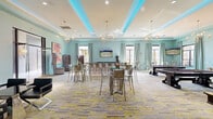 Located at 3800 SW Richsmith Rd in Bentonville, Arkansas, this generously sized single-floor community clubhouse offers an impressive array of amenity spaces united by a cohesive contemporary design aesthetic. The grand lobby welcomes visitors with marble-look tile flooring, coffered ceilings adorned with teal LED accent lighting, elegant chandeliers, and plush seating arrangements centered around a sleek linear fireplace — creating a sophisticated yet inviting first impression.

The expansive social lounge is dressed in soft aqua tones with boldly patterned carpeting in grey and yellow, high-top tables with metallic seating, flat-screen televisions, and floor-to-ceiling drapery framing multiple windows that invite natural light. A dedicated game room features billiard and shuffleboard tables alongside curated wall art. A glass-enclosed poker room with shiplap walls, a crystal chandelier, and views of the outdoors offers an intimate retreat for private gatherings.

A stylish bar area is defined by glass partition walls, herringbone hardwood-style flooring, backlit blue shelving, a rolling library ladder, and leather barstools. Private office suites with glass doors provide functional workspace, while a cozy lounge nook with a plush blue sofa and gallery-style artwork rounds out the offerings. Throughout, curated original artwork and upscale finishes elevate the overall ambiance of this thoughtfully designed clubhouse.