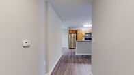 Located on Settlers Landing Road in Hampton, Virginia, this single-floor residence offers a thoughtfully designed layout with a clean, modern aesthetic throughout. The entry hallway leads into an open-concept living and kitchen area, unified by warm hardwood-style luxury vinyl plank flooring that extends across the main living spaces.

The kitchen is a functional centerpiece of the home, featuring warm honey-toned cabinetry, granite-look countertops, and a full suite of stainless steel appliances including a refrigerator, range, and over-the-range microwave. A peninsula with an integrated sink and additional counter space provides both a casual dining option and a natural division between the kitchen and the adjoining living area. The living space is bright and airy, benefiting from a sliding glass door that opens to an outdoor balcony and allows generous natural light to fill the room. Crown molding adds a refined architectural touch.

The bedroom is a generously sized retreat finished with plush carpet, neutral tones, and a charming bay window that floods the space with soft, natural light. A walk-in closet with built-in shelving provides ample storage. The bathroom is clean and well-appointed, complete with a tub-shower combination, wood-toned vanity, and coordinating flooring.
