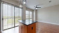 Located at 1101 Bear Creek Pkwy in Keller, TX, this single-floor residence offers a thoughtfully designed layout with modern finishes throughout. The kitchen serves as a central highlight, featuring warm wood cabinetry that extends to the ceiling for maximum storage, granite-style countertops, black appliances including a refrigerator, electric range, microwave, and dishwasher, and a double stainless steel sink with a matte black faucet. A central island with a dark granite surface and pendant lighting adds both functionality and visual appeal, seamlessly connecting the kitchen to the open living area. Rich hardwood-style flooring flows throughout the main living spaces, complemented by neutral wall tones that create a bright, welcoming atmosphere. Large windows invite generous natural light, and a ceiling fan enhances comfort in the living area. A sliding glass door opens to a balcony with outdoor views. The hallway connects the private areas of the unit, leading to carpeted bedrooms equipped with closets featuring built-in shelving. The bathroom is clean and functional, offering a tiled tub-shower combination, a wood-cabinet vanity with a white countertop, and a large mirror. Overall, the space balances contemporary design with practical livability.