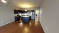 This single-floor residence is thoughtfully designed with a contemporary aesthetic and functional layout. The open-concept living and kitchen area serves as the heart of the unit, anchored by rich hardwood flooring that extends throughout the common spaces. A ceiling fan overhead complements the warm ambient lighting, while large sliding glass doors and tall windows allow generous natural light to fill the living area.

The kitchen is outfitted with dark espresso cabinetry offering abundant storage, granite countertops, and a full suite of stainless steel appliances including a refrigerator, range, built-in microwave, and dishwasher. A center island with matching granite provides additional prep space and casual seating potential. Under-cabinet lighting highlights the clean lines of the countertops.

The bedrooms feature plush carpet flooring and are well-lit by wide windows with blinds. Each room includes a sliding closet with rod and shelf storage. Neutral gray walls throughout create a versatile backdrop.

The bathroom is finished with large-format tile flooring, a dark vanity with granite countertop and undermount sink, and a full tub-shower combination with tiled surround. A small window provides natural ventilation and light.