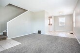 Located at 1959 Stanton St in Dubuque, Iowa, this multi-story home spans three floors and offers a practical, functional layout. The main level features a combined kitchen and living room area, where light tile flooring runs through the kitchen and transitions to carpet in the living space. Multiple windows allow natural light to fill the room, creating a bright and open atmosphere. The kitchen is equipped with warm oak cabinetry, dark granite-style countertops, a white tile backsplash, and a stainless steel sink, providing ample storage and workspace. A white electric range and a solid wood entry door with window add character to the space. A staircase connects the levels, with the upper floor housing two carpeted bedrooms, each featuring ceiling fans and windows with neighborhood views. The primary bedroom includes access to a closet and additional door, offering convenient storage. The shared full bathroom on this level features tile flooring, a pedestal sink, and a medicine cabinet mirror. The lower level serves as an unfinished utility space with a painted concrete floor, exposed ductwork, and staircase access — ideal for storage or mechanical use. Neutral gray-toned walls and consistent finishes throughout give the home a cohesive, understated aesthetic.
