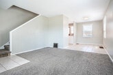 Located at 1959 Stanton St in Dubuque, Iowa, this multi-story home spans three floors and offers a practical, functional layout. The main level features a combined kitchen and living room area, where light tile flooring runs through the kitchen and transitions to carpet in the living space. Multiple windows allow natural light to fill the room, creating a bright and open atmosphere. The kitchen is equipped with warm oak cabinetry, dark granite-style countertops, a white tile backsplash, and a stainless steel sink, providing ample storage and workspace. A white electric range and a solid wood entry door with window add character to the space. A staircase connects the levels, with the upper floor housing two carpeted bedrooms, each featuring ceiling fans and windows with neighborhood views. The primary bedroom includes access to a closet and additional door, offering convenient storage. The shared full bathroom on this level features tile flooring, a pedestal sink, and a medicine cabinet mirror. The lower level serves as an unfinished utility space with a painted concrete floor, exposed ductwork, and staircase access — ideal for storage or mechanical use. Neutral gray-toned walls and consistent finishes throughout give the home a cohesive, understated aesthetic.