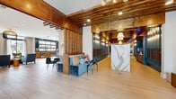 Located at 4428 White Birch Avenue in Smyrna, Tennessee, this impressive single-floor community clubhouse offers an expansive and thoughtfully designed gathering space. The grand entrance welcomes visitors through large glass doors beneath a striking mid-century modern chandelier, opening into a bright, airy foyer with light wood-plank flooring that flows seamlessly throughout the entire space.

The main lobby area showcases exposed wooden beam ceilings with warm, rustic tones contrasted against crisp white walls, creating a sophisticated industrial-chic aesthetic. A stunning marble-veined reception island serves as a focal point, flanked by rows of built-in mailboxes finished in deep teal cabinetry. Cozy seating nooks with velvet sofas and accent chairs invite relaxed conversation.

The lounge areas feature coffered ceilings, oversized pendant lighting, and abundant natural light streaming through floor-to-ceiling windows and sliding glass doors. A built-in window bench with wood surround and dark stone accent wall adds an intimate, functional touch to the hallway.

The kitchen and living area is anchored by a large island with leather bar seating, complemented by bold black-and-gold pendant lights, warm wood cabinetry, stainless steel appliances, and an industrial-style roll-up window that opens to the outdoors. A billiards area and multiple seating vignettes complete this versatile, amenity-rich space.