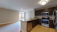This well-appointed single-floor residence offers a thoughtfully designed open-concept layout that seamlessly connects the kitchen and living areas. The kitchen is a standout feature, showcasing dark espresso cabinetry, granite countertops with warm tonal variation, and a full suite of stainless steel appliances including a GE electric range, over-the-range microwave, dishwasher, and refrigerator. A peninsula counter provides additional prep space and serves as a natural divider between the kitchen and the expansive living area.

The living space is bright and airy, with light hardwood flooring throughout and large French doors that open to a private balcony, inviting an abundance of natural light. Neutral-toned walls complement the clean, modern aesthetic across the unit.

The bedrooms are carpeted for comfort, with generous windows that allow natural light to filter in, and each room offers ample space for furnishings. The bathroom is finished with dark wood-grain floating vanity cabinetry, a white countertop, large wall mirrors, and tile flooring, maintaining the modern design language found throughout the unit.

Additional interior features include multiple closets and a practical, well-connected hallway layout. The overall ambiance is clean, contemporary, and move-in ready.
