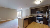 This well-appointed single-floor residence offers a thoughtfully designed open-concept layout that seamlessly connects the kitchen and living areas. The kitchen is a standout feature, showcasing dark espresso cabinetry, granite countertops with warm tonal variation, and a full suite of stainless steel appliances including a GE electric range, over-the-range microwave, dishwasher, and refrigerator. A peninsula counter provides additional prep space and serves as a natural divider between the kitchen and the expansive living area.

The living space is bright and airy, with light hardwood flooring throughout and large French doors that open to a private balcony, inviting an abundance of natural light. Neutral-toned walls complement the clean, modern aesthetic across the unit.

The bedrooms are carpeted for comfort, with generous windows that allow natural light to filter in, and each room offers ample space for furnishings. The bathroom is finished with dark wood-grain floating vanity cabinetry, a white countertop, large wall mirrors, and tile flooring, maintaining the modern design language found throughout the unit.

Additional interior features include multiple closets and a practical, well-connected hallway layout. The overall ambiance is clean, contemporary, and move-in ready.