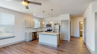 This well-appointed single-floor unit offers a contemporary design with a cohesive neutral palette and rich hardwood-style flooring carried throughout. The open-concept kitchen serves as the heart of the space, showcasing light gray cabinetry, white quartz countertops, a classic subway tile backsplash, and a full suite of stainless steel appliances including a range, microwave, dishwasher, and refrigerator. A central island provides additional prep and seating space, while stylish pendant lighting adds a modern finishing touch overhead. The living area benefits from direct outdoor access through glass French doors, allowing natural light to fill the room, complemented by a ceiling fan for year-round comfort. The bedrooms are generously sized, each featuring ceiling fans and windows fitted with blinds that frame views of the surrounding greenery. A hallway connects the private rooms, maintaining a clean separation between living and sleeping areas. The bathrooms are finished with white vanities featuring quartz countertops and gray cabinetry, with one bathroom offering a full tub-shower combo. The primary bath includes an adjacent walk-in closet with built-in shelving and hanging space, adding practical storage. The overall design is clean, modern, and move-in ready.