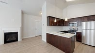 This single-floor residence offers a thoughtfully designed open layout that balances functionality with modern aesthetics. The kitchen serves as a central highlight, featuring rich dark espresso cabinetry with brushed nickel hardware, light quartz countertops, a peninsula with an undermount double sink, and a full suite of stainless steel appliances including a gas range, built-in microwave, dishwasher, and refrigerator. Pendant lighting hangs above the peninsula, complementing the dramatic vaulted ceilings that add a sense of spaciousness to the kitchen and adjoining areas.

The living area continues the vaulted ceiling design and is anchored by a classic fireplace with a white surround. Large windows and a glass-panel exterior door flood the space with natural light, while a ceiling fan provides year-round comfort. Light wood-style flooring runs seamlessly throughout the main living areas, creating a clean and cohesive look.

The bedroom is carpeted and features a window with blinds and a ceiling fan. The bathroom is well-appointed with dark vanity cabinetry, a white quartz countertop, and a full tub-shower combination with white tile surround. A dedicated in-unit laundry area accommodates a stacked washer and dryer, adding everyday convenience to this efficiently designed space.