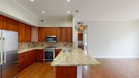 This single-floor residence offers a well-organized layout comprising two bedrooms, three bathrooms, a combined kitchen and living area, a closet, and a hallway. The kitchen is a standout feature, showcasing rich cherry wood cabinetry extending to the ceiling, granite countertops with warm veining, a stone tile backsplash, and a suite of stainless steel appliances including a gas range, built-in microwave, and a side-by-side refrigerator. A peninsula with additional granite countertop space provides extra prep area and is accented by stylish pendant lighting overhead. Hardwood flooring runs throughout the main living and kitchen areas, adding warmth and continuity. The generously sized primary bedroom features plush carpeting, crown molding, multiple windows with outdoor tree views, and a walk-in closet outfitted with dual hanging rods and shelving. The second bedroom also offers carpeted flooring, crown molding, and an arched window that fills the room with natural light. The bathrooms are finished with tile flooring and surrounds, granite-topped vanities with wood cabinetry, and soaking tub options—including a deep, oversized tub in one bath. Crown molding is a consistent architectural detail throughout, adding a refined touch to the overall aesthetic.