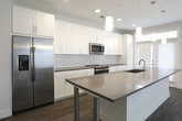 This single-floor residence at 5775 Glenridge Drive NE in Sandy Springs, Georgia, presents a clean, contemporary design with a well-planned open layout. The living and kitchen areas share a cohesive flow, unified by warm-toned wood-look flooring throughout. The kitchen is a standout feature, equipped with white shaker cabinetry extending to the ceiling, a classic subway tile backsplash, stainless steel appliances including a French door refrigerator and gas range, and a large island with a neutral quartz-style countertop and undermount sink. Pendant lighting above the island adds a refined touch, complementing the recessed lighting overhead.

The living area is generously proportioned, with a ceiling fan and ample wall space. A set of double doors provides access to additional storage or utility space within the unit. Bedrooms are carpeted for comfort, with one room featuring glass doors that invite natural light. The primary bedroom connects to a walk-in closet outfitted with wire shelving and hanging rods, as well as an en-suite bath featuring a glass-enclosed shower with white tile surround. A secondary full bathroom offers a tub-shower combination and wood-look tile flooring, maintaining the unit's consistent modern aesthetic throughout.