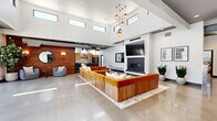 This contemporary single-floor space is defined by its striking architectural design and open, airy layout. Soaring ceilings with a row of clerestory windows flood the interior with abundant natural light, while polished concrete floors extend seamlessly throughout, lending an industrial-modern aesthetic.

The expansive main lounge serves as the centerpiece, featuring a large sectional sofa in warm amber upholstery with wood-panel base detailing, anchored by a patterned area rug. A sleek fireplace with a dark tile surround and a wall-mounted flat-screen television create a refined focal point. Decorative pendant lighting hangs overhead, adding character to the double-height volume.

A cozy seating nook along a richly textured reclaimed wood accent wall offers a more intimate retreat, complete with soft grey armchairs, a round decorative mirror, and lush greenery. Adjacent to this area, the fully equipped kitchen features light wood cabinetry, white subway tile backsplash, stainless steel appliances, a central island with bar seating, and a wall-mounted counter with bar stools.

Floor-to-ceiling black-framed glass walls open visually onto a landscaped outdoor pool deck, providing sweeping views of the surrounding trees and mountains. A wall-mounted Scrabble board and motivational artwork add playful, personalized touches throughout the space.