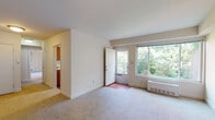 This single-floor residence is designed with a practical and comfortable layout. The living area is a welcoming, open space finished with wall-to-wall carpeting and crisp white walls. A large sliding window frames lush green tree views, filling the room with natural light. A secondary door provides direct outdoor access, and a baseboard heating unit ensures year-round comfort. The entry foyer features hardwood-style flooring, creating a clear transition from the exterior into the living space.

The kitchen is efficiently laid out and equipped with warm wood cabinetry offering generous upper and lower storage. White appliances, including an electric range, microwave, and dishwasher, complement the light countertops. A stainless steel sink is positioned beneath a window, providing natural light while cooking. Hardwood-style flooring runs throughout the kitchen.

The bedroom is a comfortable, carpeted room with a ceiling fan for climate control and a set of double doors leading to a closet. The room connects conveniently to the rest of the unit.

The bathroom features a full-size bathtub with a shower, a vanity with an integrated sink set in wood cabinetry, and a frosted window that allows natural light while maintaining privacy. The overall ambiance of this residence is clean, functional, and well-lit throughout.