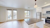 This 2-bedroom, 1-bathroom unit at 23040 Military Rd in Kent, WA offers a well-designed layout with modern finishes and practical features throughout. Light hardwood-style flooring runs through the main living areas, complementing the bright, white walls and clean aesthetic of the space.

The kitchen is a standout feature, equipped with stainless steel appliances, white shaker-style cabinetry, a glass tile backsplash, dark quartz countertops, and a central island with pendant lighting — ideal for both cooking and casual dining. The adjacent living room is bathed in natural light from multiple windows and offers direct access to a private balcony with outdoor views, with a ceiling fan adding comfort.

Both bedrooms are carpeted and include ceiling fans, providing a cozy and quiet retreat. The primary bedroom offers a comfortable footprint with a closet and easy access to the full bathroom. The bathroom features a wide vanity with dual sinks, dark countertops, white cabinetry, and a full soaking tub. A dedicated in-unit stacked washer and dryer adds everyday convenience. A stylish sliding barn door and well-placed closets round out the functional and thoughtfully arranged design of this modern unit.