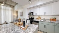 Located at 888 N Fourth St in the heart of downtown Phoenix, this contemporary one-bedroom, one-bathroom residence offers a well-designed, efficient layout with modern industrial-inspired finishes. The open-concept living and kitchen area is a standout feature, anchored by a granite-topped island with bar seating — ideal for casual dining or entertaining. The kitchen is outfitted with stainless steel appliances, a stainless steel refrigerator, a built-in microwave, a dishwasher, and a two-toned cabinetry scheme pairing crisp white upper cabinets with sage green lower cabinets, all accented by sleek matte black hardware. Polished concrete floors run throughout the space, lending an urban, loft-like aesthetic. The living room is bright and airy, benefiting from floor-to-ceiling windows with sheer vertical blinds that invite abundant natural light. The bedroom offers a calm retreat with access to both the closet and bathroom, maintaining a practical and connected flow. The bathroom features granite countertops, a full soaking tub with shower, and polished concrete floors consistent with the rest of the home. Exposed concrete architectural elements and track lighting add to the space's contemporary character throughout.