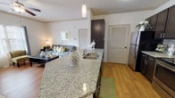 This single-floor residence in Bossier City, Louisiana offers a thoughtfully designed open-concept layout with a cohesive, modern aesthetic throughout. The kitchen is well-equipped with dark espresso cabinetry, granite countertops, stainless steel appliances, and a large island with a built-in sink — ideal for both cooking and casual entertaining. Warm hardwood flooring runs seamlessly throughout the space, enhancing the inviting atmosphere.

The living area flows naturally from the kitchen, featuring crown molding and ample room for comfortable seating. Adjacent to the living room, the dining area benefits from generous natural light through large windows and a sliding glass door, creating a bright and welcoming setting for meals.

The bedroom is a restful retreat, complete with a ceiling fan, a window with outdoor views, and well-proportioned space for furnishings. A hallway connects the living spaces and bedroom, punctuated by tasteful wall art that adds warmth to the transition areas.

The bathroom mirrors the design language of the kitchen, showcasing matching dark cabinetry, granite countertops, a large vanity mirror, and hardwood flooring. A louvered pantry or utility door adds a classic architectural touch to the kitchen corridor. Crown molding and neutral wall tones throughout lend the entire residence a polished, cohesive finish.