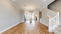 Located at 17014 Fairmount Way in Pineville, NC, this two-story home offers a well-designed layout across two floors. The main level features an open-concept kitchen and living area with warm hardwood-style flooring, crown molding, and recessed lighting. The kitchen is a standout, showcasing white shaker cabinetry extending to the ceiling with glass-front upper cabinets, stainless steel appliances, a subway tile backsplash, and a large center island with a white countertop and pendant lighting. The living area flows seamlessly from the kitchen, filled with natural light from multiple windows. A convenient half bathroom with hardwood-style flooring is also located on the main level. A classic white-railed staircase leads to the upper floor, where two bedrooms are found. The generously sized primary bedroom features plush carpeting, a ceiling fan, and ample natural light. A walk-in closet with built-in shelving and hanging rods provides excellent storage. The upper level also hosts well-appointed bathrooms, including one with a tiled tub-surround, white vanity, and elegant framed mirror. Neutral warm-toned walls and crisp white trim are consistent throughout, giving the home a clean, cohesive aesthetic.
