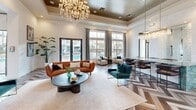 This opulent 1690 square foot space, situated in Las Vegas' Southern Highlands, exemplifies modern luxury and versatile design. The single-story layout boasts a grand entrance with soaring ceilings adorned by a striking coffered design and pendant lighting. The flooring throughout is a stunning chevron-patterned hardwood, adding visual interest and sophistication.

The space is divided into multiple recreational areas, each designed for specific purposes. A billiards room features a elegant white pool table, while the lounge area is furnished with plush seating and a sleek flat-screen TV. The focal point of the main living area is a dramatic white brick wall housing a linear fireplace and built-in shelving, perfect for displaying decorative items.

Large glass doors and windows flood the space with natural light and offer views of an outdoor pool area. The interior is further illuminated by an array of lighting fixtures, including a grand crystal chandelier and contemporary linear chandeliers.

The color palette is predominantly neutral, with white walls and warm wood tones, accented by pops of color in the furnishings. Thoughtful decor elements, such as potted plants and artistic pieces, add warmth and personality to the space.

This multifunctional community area seamlessly blends comfort with sophistication, providing residents with a luxurious environment for relaxation and social gatherings.