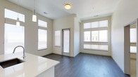Located at 4470 South Lemay Avenue in Fort Collins, Colorado, this single-floor residence offers a clean, modern aesthetic with an open and airy layout. The living area is bathed in natural light, thanks to an abundance of large windows fitted with roller shades, which frame views of the surrounding neighborhood while allowing for adjustable privacy. Tall ceilings amplify the sense of space, contributing to the unit's bright and welcoming atmosphere. Rich, dark hardwood-style flooring runs throughout the main living space, providing a striking contrast against the crisp white walls and neutral-toned finishes. A glass-paneled door leads to an outdoor access point, seamlessly connecting the interior to the exterior. The kitchen area features sleek white countertops, visible from the living space, reinforcing the home's contemporary design language. Pendant lighting adds a stylish accent, complementing the flush-mount ceiling fixtures. The overall ambiance is one of understated modern elegance — well-suited for those seeking a functional yet refined living environment in one of Fort Collins' accessible south-side locations.