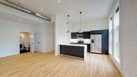 This single-floor unit showcases a thoughtfully designed open-concept layout that seamlessly integrates living and kitchen areas. The kitchen serves as the centerpiece, featuring sleek, dark flat-front cabinetry paired with stainless steel appliances, including a gas range, microwave, and French door refrigerator. A substantial island with a white countertop and undermount sink provides both workspace and a natural gathering point, illuminated by modern pendant lights. Exposed industrial ductwork adds a loft-like character to the soaring ceilings.

Light hardwood flooring runs consistently throughout the unit, connecting each space cohesively. Tall, large-pane windows flood the living areas with natural light and frame street-level urban views, complemented by a whitewashed exposed brick accent wall. A well-proportioned hallway with louvered closet doors leads to the bedrooms, each offering hardwood floors, black-framed windows with outdoor views, and generous closet space, including a walk-in configuration.

The bathrooms are finished with white hexagonal mosaic tile surrounding soaking tubs, dark floating vanities with white countertops, and slate-toned floor tile, combining classic and contemporary design elements throughout.