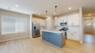 This single-story home showcases a thoughtfully designed open-concept layout with consistent light wood-tone flooring flowing throughout the main living areas. The kitchen serves as the centerpiece, featuring crisp white shaker cabinetry, a classic white subway tile backsplash, and a striking blue-paneled island with a white countertop and integrated sink. Pendant lighting above the island adds warmth, while stainless steel appliances — including a gas range, built-in microwave, and french door refrigerator — complete the contemporary look. Recessed lighting and a window provide additional brightness throughout.

The open living area extends from the kitchen, offering a welcoming gathering space with a fireplace visible in the background. Bedrooms are carpeted in a neutral tone and receive natural light through windows with horizontal blinds. The primary suite connects to a bathroom with a walk-in glass-enclosed shower and an adjoining walk-in closet with wire shelving. A secondary full bathroom features a white vanity with dark hardware, a tub-shower combo, and light wood flooring. The home's neutral color palette and clean finishes create a cohesive, move-in ready aesthetic throughout.