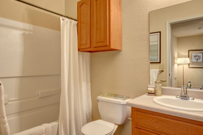 A bathroom with a tub, wall storage, and wide mirror over the sink - The Residence at Heritage Park