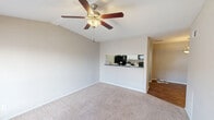 Located at 1111 Queens Rd in Pasadena, TX, this one-bedroom, one-bathroom unit offers a practical and well-organized single-floor layout. The living room is a standout feature, boasting vaulted ceilings that lend a sense of openness beyond the unit's compact footprint. A ceiling fan with a light fixture is centrally installed, providing both airflow and illumination. Natural light enters through a window fitted with blinds, and the entry door opens directly into this space. Soft carpet covers the living area floor, transitioning to hardwood-style flooring at the entryway. An open pass-through connects the living room to the galley-style kitchen, which features white cabinetry, dark countertops, and black appliances including a refrigerator, electric range, microwave, and dishwasher, all set on durable hardwood-style flooring. The bedroom is a comfortable, carpeted room with a ceiling fan, a window for natural light, and two closets offering ample storage. The bathroom includes a full tub-shower combination with a curtain rod, a toilet, and hardwood-style flooring, finished with neutral-toned walls throughout. The unit's consistent warm, neutral palette and functional design make for a cohesive and livable space.