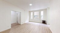 Located at 3333 W 4th St in Los Angeles, CA, this single-floor unit offers a clean, modern aesthetic defined by bright white walls, light hardwood flooring, and a well-considered layout. The combined kitchen and living room serves as the heart of the space, with the living area bathed in natural light from three tall, narrow windows framed in crisp white trim. A classic cast-iron radiator adds a charming vintage touch beneath the windows, complementing the otherwise contemporary finish. The galley-style kitchen is thoughtfully appointed with white shaker cabinetry extending from floor to ceiling on both sides, providing generous storage. Light quartz countertops, a stainless steel undermount sink with a sleek pull-down faucet, a stainless steel gas range, and a full-size stainless steel refrigerator complete the kitchen's functional and stylish design. The living area offers an open, unobstructed floor plan that allows for flexible furniture arrangements. A connecting hallway links the main living space to the entry, maintaining a logical and efficient flow throughout the unit. The overall ambiance is fresh, light-filled, and move-in ready, reflecting a thoughtfully updated interior well-suited to urban living in the Koreatown neighborhood of Los Angeles.