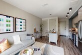 This thoughtfully designed single-floor residence combines contemporary style with functional living. The galley kitchen is a standout feature, outfitted with stainless steel appliances including a French door refrigerator, gas range, and built-in microwave, complemented by two-tone cabinetry, a geometric tile backsplash, and a undermount sink with a matte black faucet. Wood-look flooring flows seamlessly from the kitchen into the open living area, where large floor-to-ceiling windows invite abundant natural light and offer views of the surrounding cityscape. A ceiling fan adds to the comfort of the airy living space, which connects effortlessly to a compact dining or work area.

The bedroom is a serene retreat, featuring plush carpeting, oversized windows framing treetop and city views, and direct access to a well-appointed walk-in closet with built-in shelving and a hanging rod. The en-suite bathroom impresses with a dual-sink vanity topped in quartz, wood-grain cabinetry, matte black hardware, and backlit LED mirrors that lend a spa-like ambiance. Throughout the residence, a neutral color palette, clean lines, and modern finishes create a cohesive and sophisticated living environment.